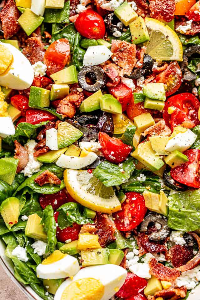 close up top view shot of boiled egg wedges, lemon slices, chopped avocados, tomatoes, and bacon set over leafy lettuce