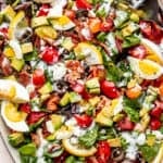 top view shot of boiled egg wedges, lemon slices, chopped avocados, tomatoes, and bacon set on top of baby spinach leaves and salad greens