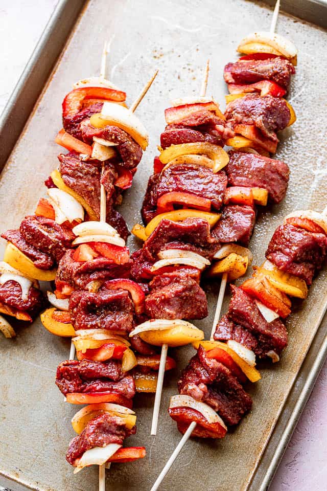 raw steak and vegetables threaded on bamboo skewers and set over a silver baking sheet