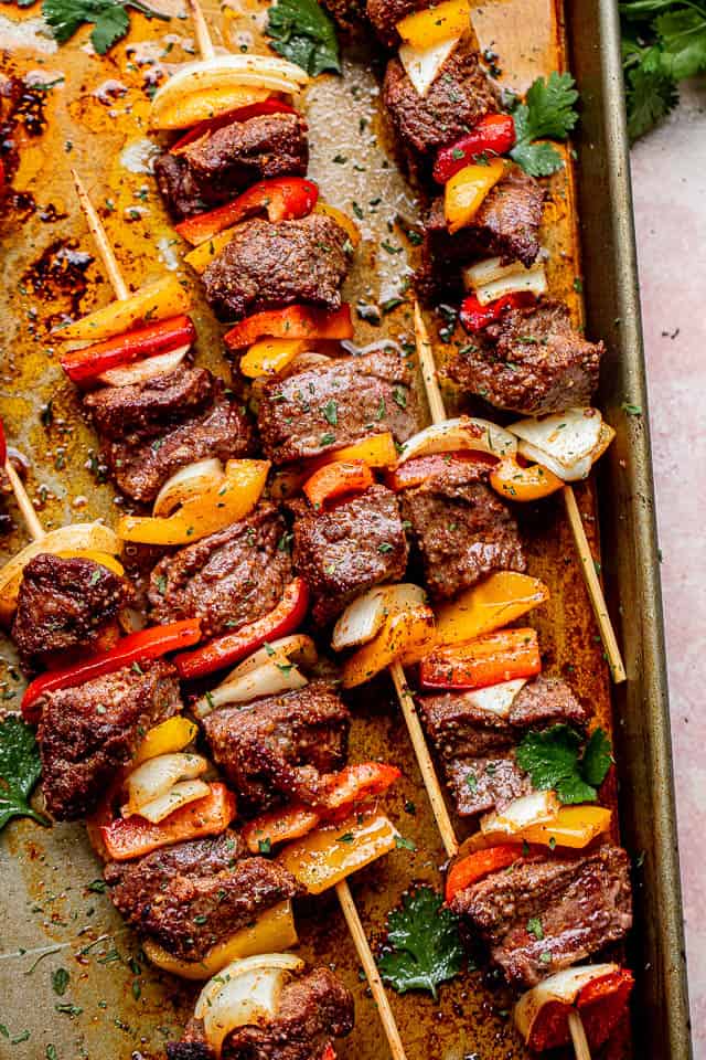 top view of oven broiled kabobs layered with top sirloin steak, onions, and peppers, and garnished with cilantro leaves 