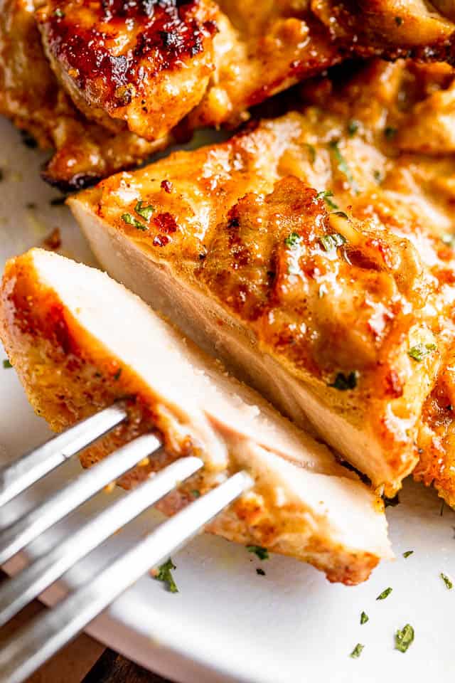 cutting a slice off cooked chicken thighs and holding it in place with a fork