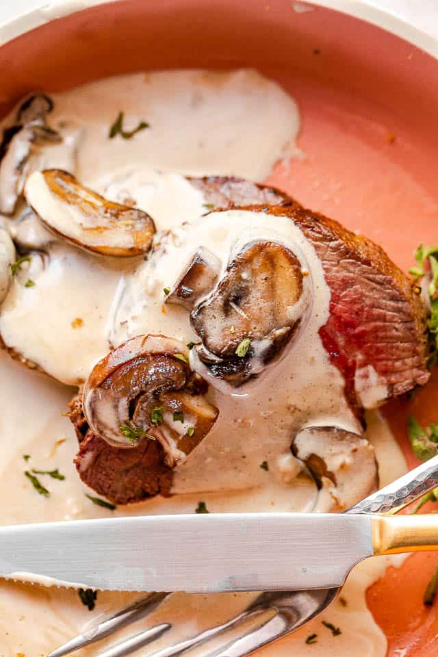 mushroom gravy over slices of beef tenderloin served on an orange plate with knife and fork