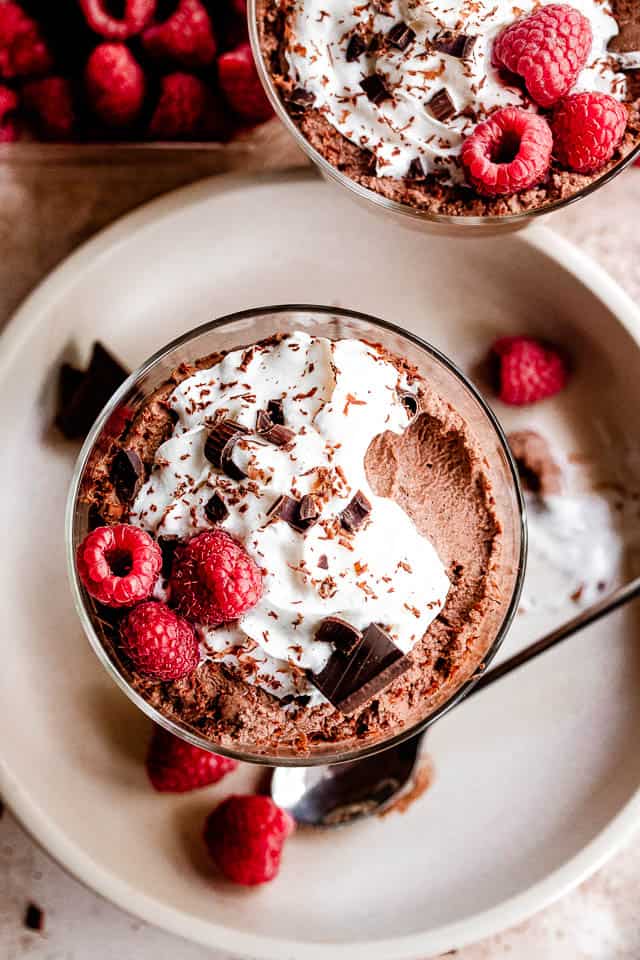 top shot of dessert dish filled with chocolate mousse, topped with whipped cream, raspberries, and chocolate shavings