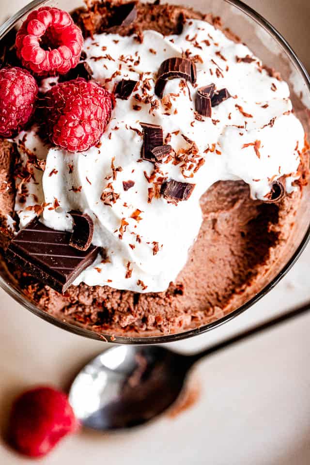 dessert dish filled with chocolate mousse, topped with whipped cream, raspberries, and chocolate shavings