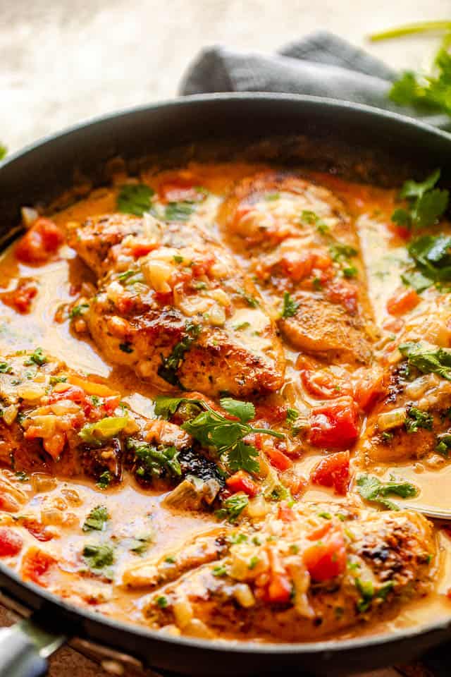 side view of chicken breasts in coconut milk sauce with diced tomatoes, onions, and cilantro