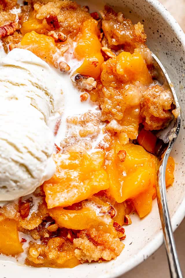 PEACH dump cake in a bowl topped with ice cream