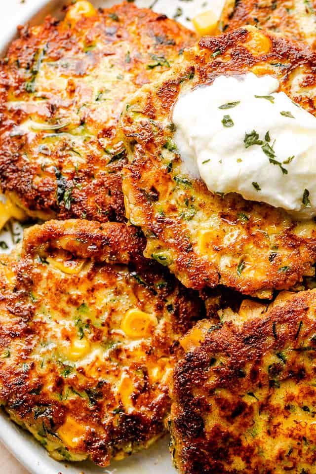 close up top shot of arranged corn zucchini fritters on a plate and topped with a dollop of yogurt dip
