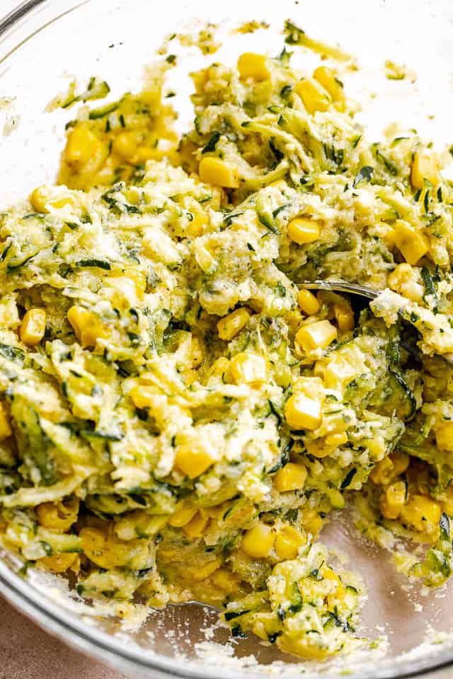 A mix of shredded zucchini and corn in a glass mixing bowl.