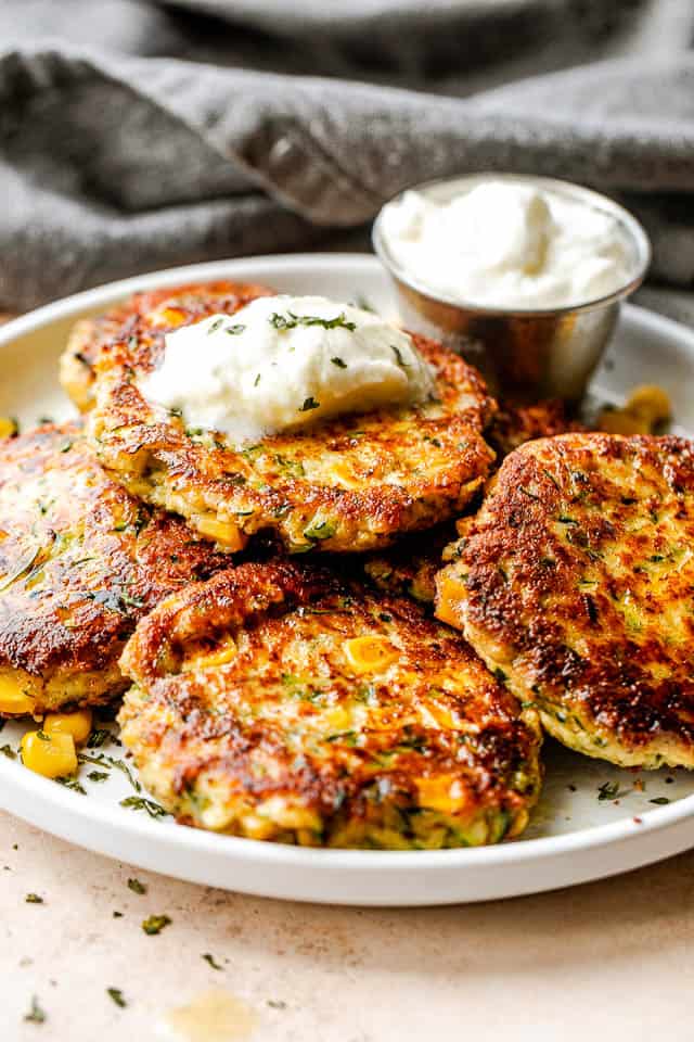 Side shot of arranged corn zucchini fritters on a plate and topped with a dollop of yogurt dip.