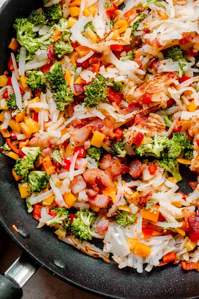 black skillet filled with hashbrowns, diced bell peppers, and small broccoli florets