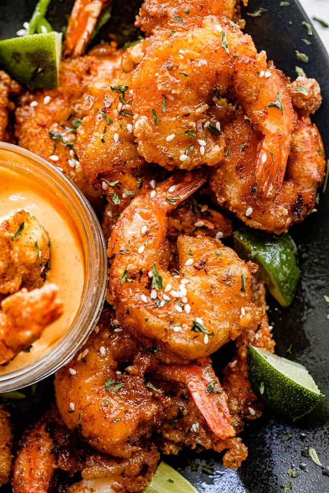 Top shot of bang bang shrimp topped with sesame seeds and served in a black plate.