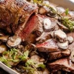 Sliced beef tenderloin on a serving plate topped with mushroom gravy.