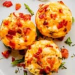 top view of three breakfast egg muffins topped with crispy bacon and set on a white plate