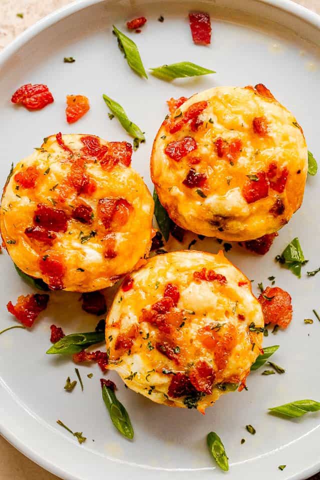 top view of three breakfast egg muffins topped with crispy bacon and set on a white plate