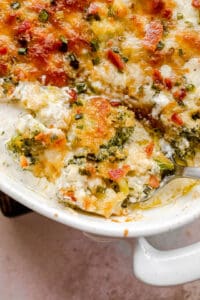 overhead shot of scooping out cheesy broccoli casserole from baking dish