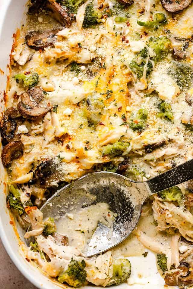 overhead close up shot of chicken broccoli casserole with a serving spoon inside the baking dish