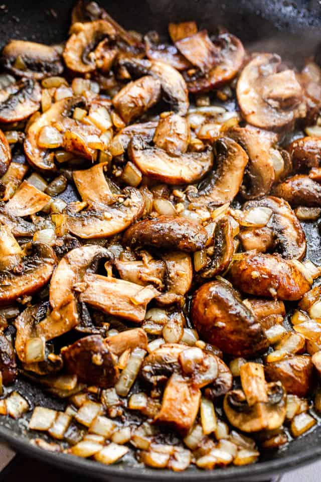 Cooking baby portobello mushrooms in a black skillet.