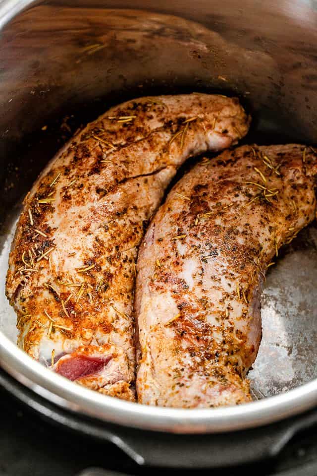 Two browned pork tenderloins inside the insert of a pressure cooker.