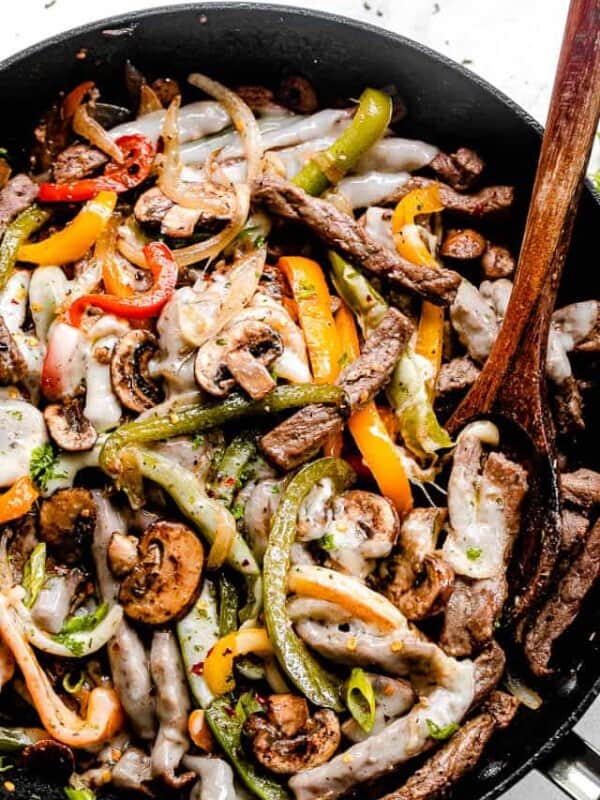 a top overhead shot of strips of peppers and steak in a black skillet with brown wooden spoon mixing the ingredients