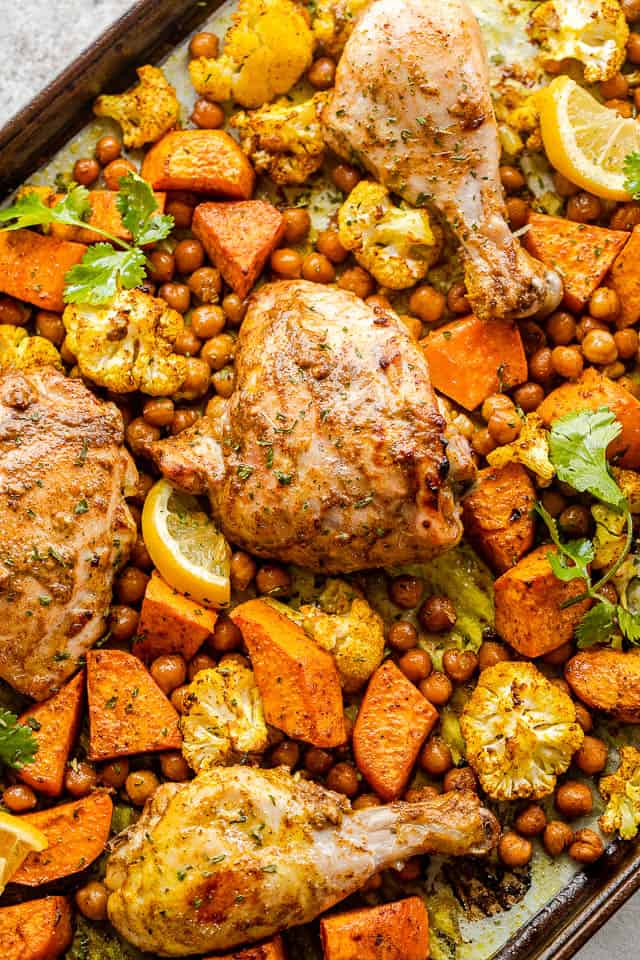 sheet pan with cooked chicken thighs, drumsticks, sweet potatoes, cauliflower florets, and chickpeas