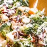 side shot of tossing broccoli apple salad with wooden salad forks