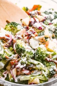 side shot of tossing broccoli apple salad with wooden salad forks