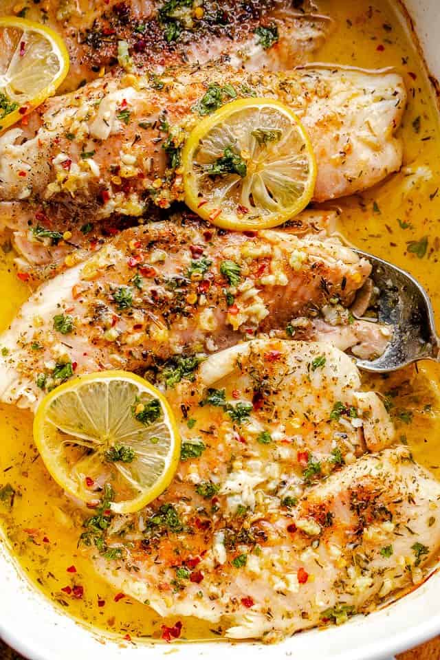 overhead shot of baked tilapia in baking dish topped with garlic and lemon slices