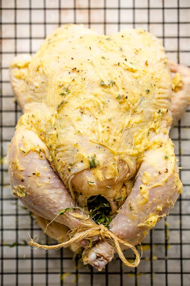 raw whole chicken rubbed with butter and tied at the legs