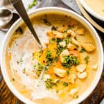 overhead up-close shot of a white bowl with cauliflower cheese soup topped with croutons and cheese