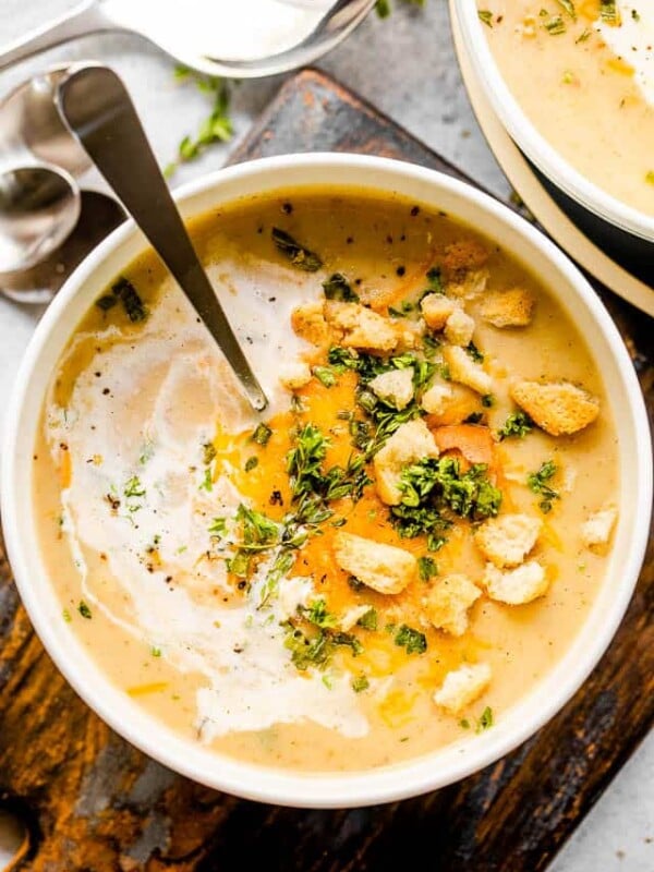 overhead up-close shot of a white bowl with cauliflower cheese soup topped with croutons and cheese