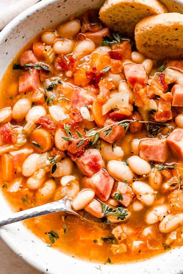 overhead shot of spoon in a white bowl filled with ham and bean soup