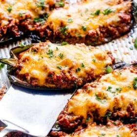 Stuffed poblano peppers filled with chili and topped with melted cheese, with a spatula slid underneath one of the peppers.