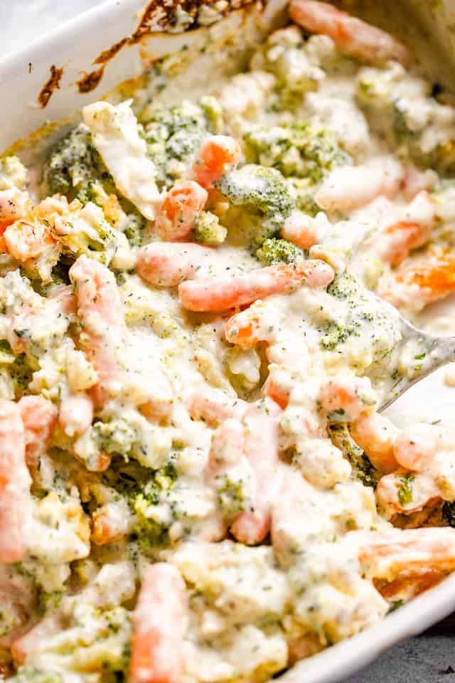 Close-up shot of cooked vegetable casserole with broccoli, carrots, and cauliflower in a baking dish.
