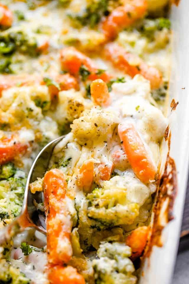 Overhead close-up shot of cooked broccoli, carrots, and cauliflower in a baking dish.