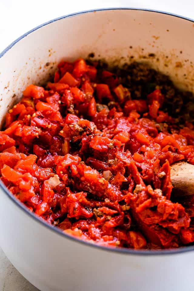 Diced tomatoes cooking in a white pot.