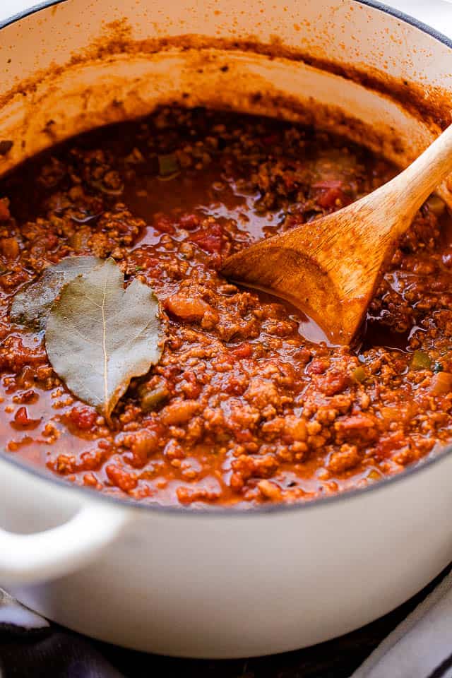 side shot of a white dutch oven filled with no beans chili and garnished with bay leaves