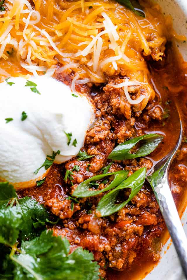 Close-up shot of Texas chili in a bowl garnished with sour cream, onions, cilantro, and shredded cheese.