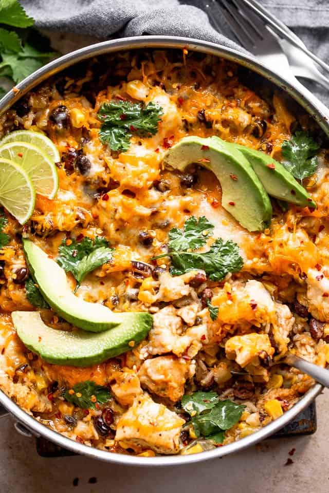 overhead shot of a skillet with salsa verde chicken and rice casserole garnished with avocado, limes, and cilantro