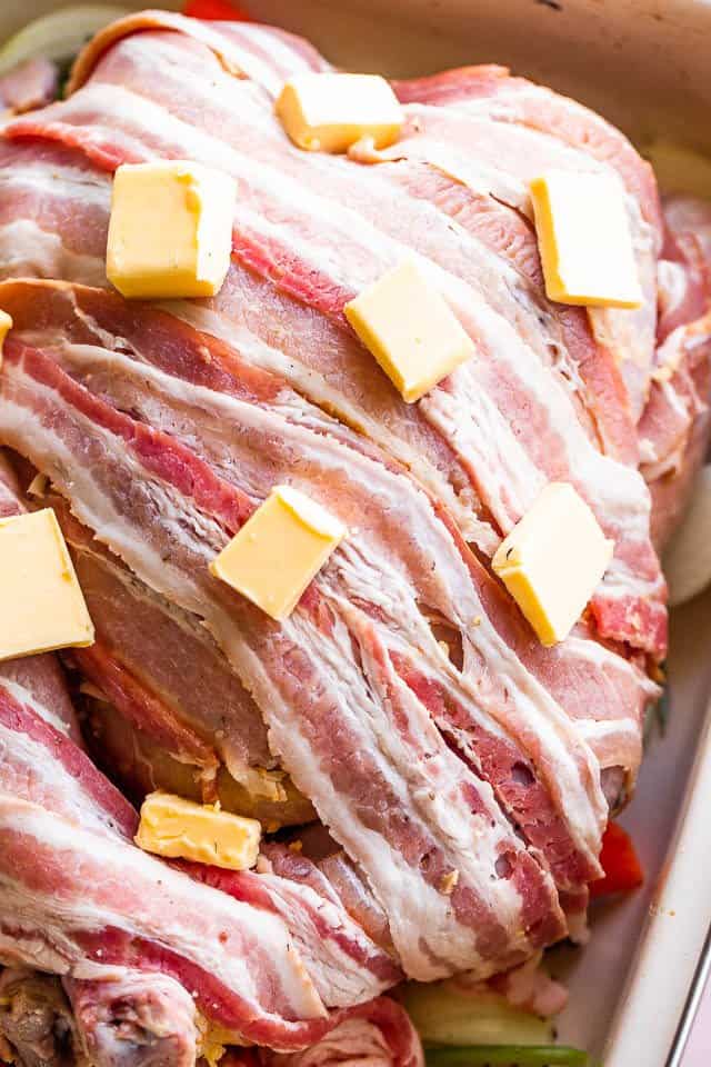 raw bacon covered turkey with butter cubes on top