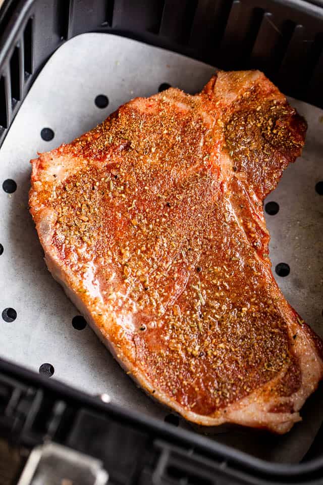 raw seasoned steak in the air fryer basket