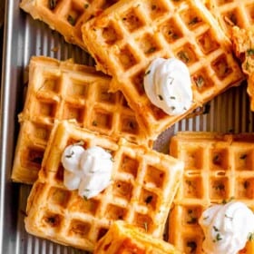 overhead shot of a number of chaffles placed on a baking sheet and topped with dollops of sour cream