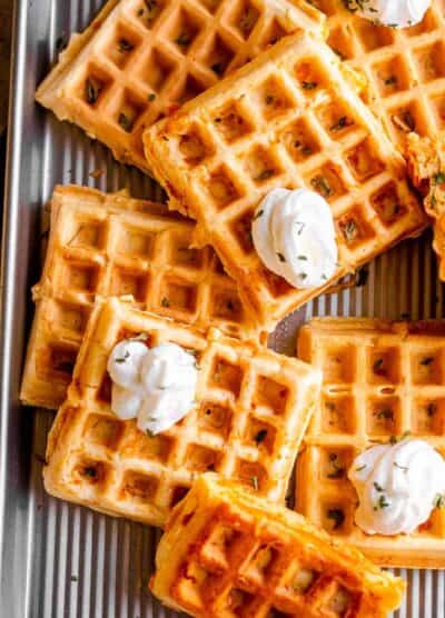 overhead shot of a number of chaffles placed on a baking sheet and topped with dollops of sour cream