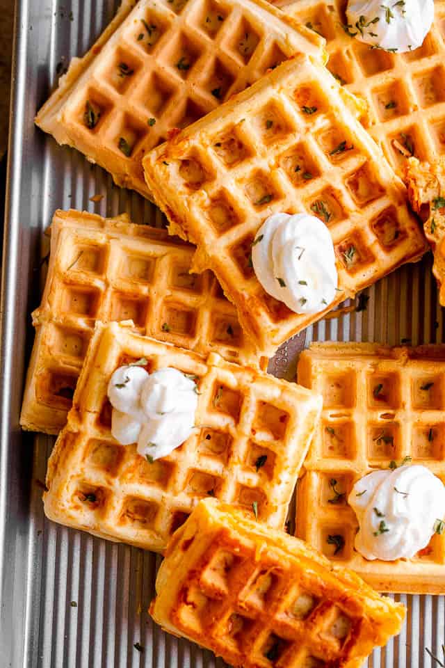 overhead shot of a number of chaffles placed on a baking sheet and topped with dollops of sour cream