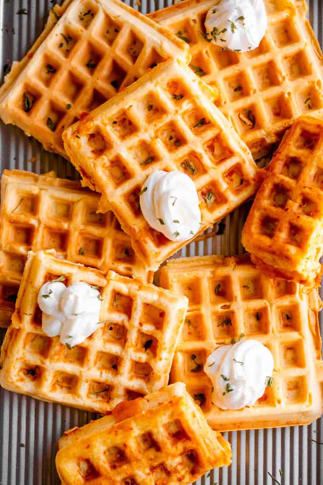 overhead shot of a number of chaffles placed on a baking sheet and topped with dollops of sour cream