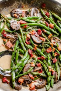 green beans and mushrooms cooking in a creamy parmesan sauce and topped with diced bacon