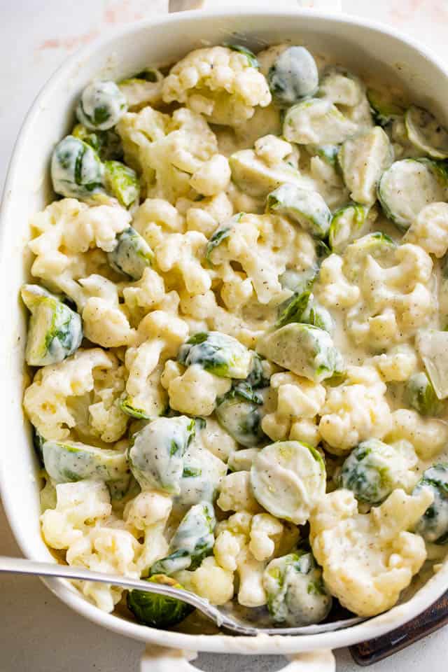 cauliflower florets and brussel sprouts in a baking dish tossed with a cheese sauce
