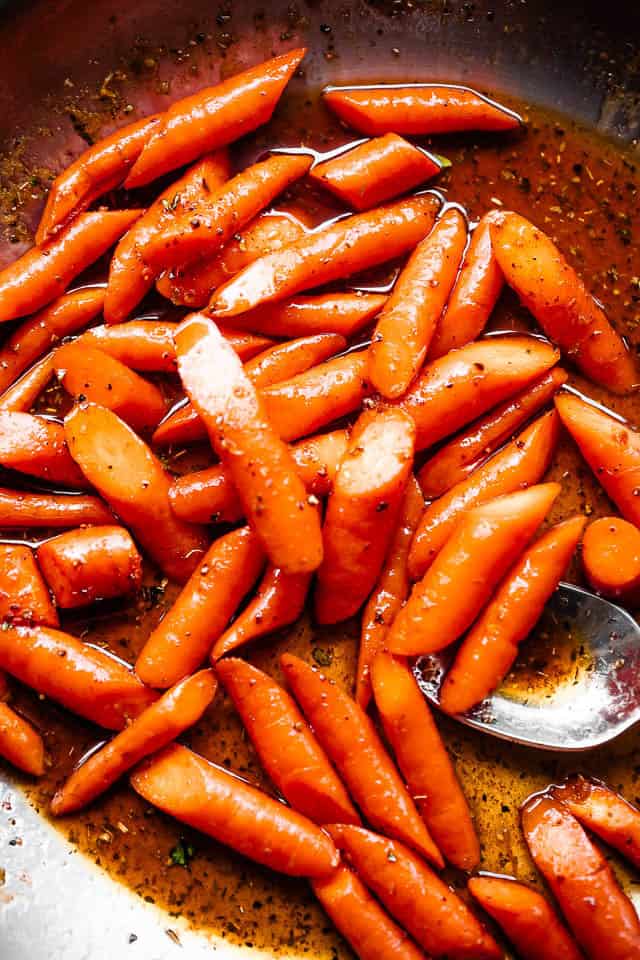 Spoon stirring through carrots in a skillet.