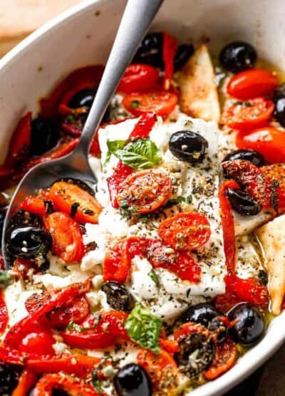 side shot of a baking dish with baked feta cheese, tomatoes, olives, and red peppers