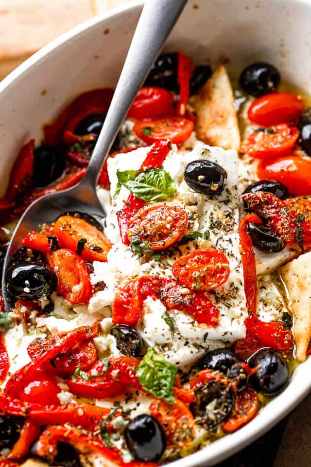 Close-up shot of a baking dish with baked feta cheese, tomatoes, olives, and red peppers