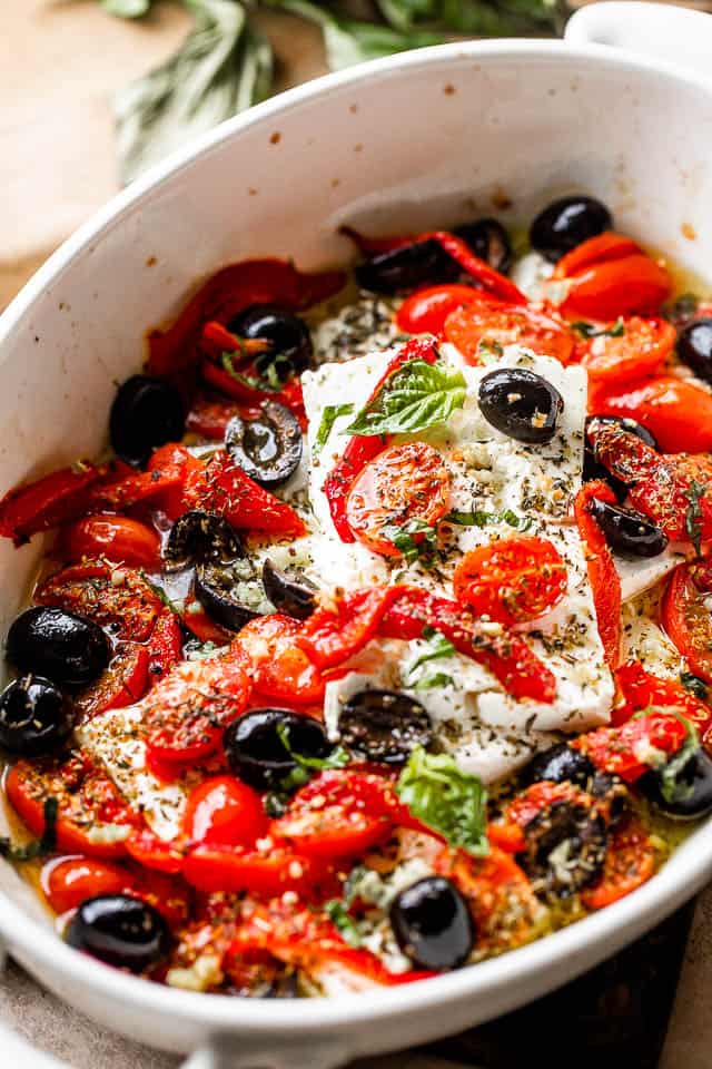 Feta cheese block topped with red pepper strips, tomatoes, olives, and herbs.